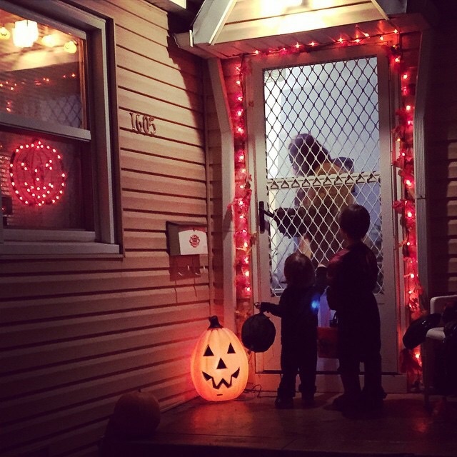 Two kids trick-or-treating at the front door of a house decorated for Halloween.