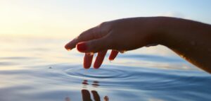 A hand hovering over quiet waters as a slow ripple meets their finger gently touching the surface