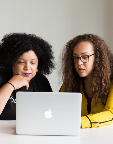 Two people sitting side by side in front of a laptop discussing motivational interview training.